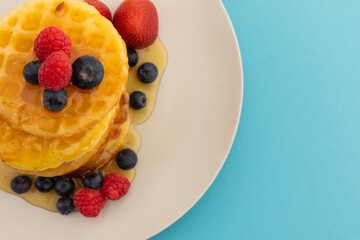 Stack of pancakes with berries and honey on plate on blue background