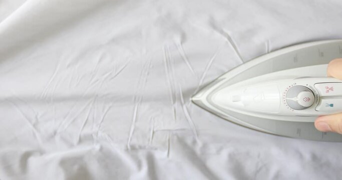 Man hand irons white clothes with a steam iron on an Ironing board. Top view. 