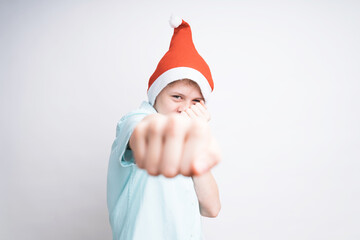 A playful Caucasian boy in Santa Claus hat is fighting, fist on the foreground