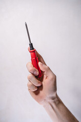 Male hand holding a Phillips screwdriver with a red handle