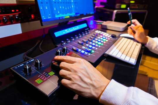 producer, editor hand tweaking volume knob on audio interface for monitoring audio signal from computer while mixing audio track on  video footage in post production studio 