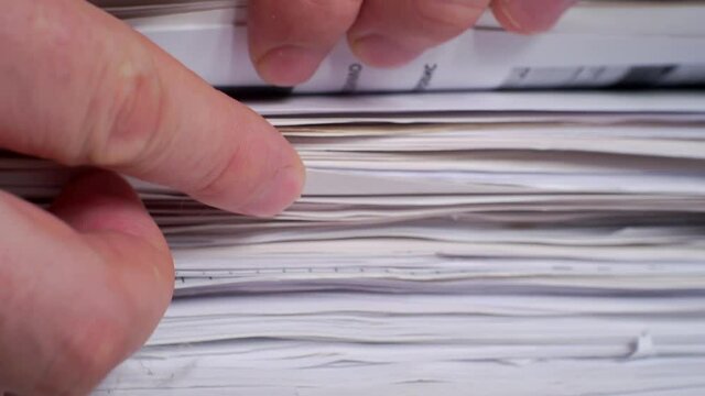 Information search.Fingers plucking through a large stack of paper documents.