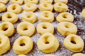 Close up of raw round donuts on table with flour before frying.