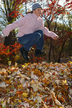Girl taking a running jump into a pile of leaves in the Fall
