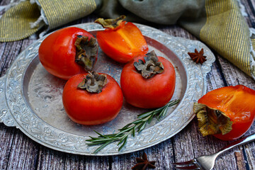 Close-up of sweet, ripe persimmons and rosemary sprigs on a silver platter.