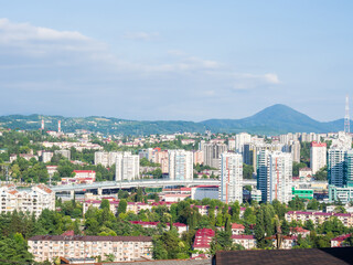 Cityscape with low and high residential buildings, flyover and green trees against the background of hills and blue sky