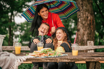 Beautiful mother with two kids are having picnic together, while it is raining.