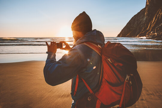 Man travel with backpack taking photo using smartphone camera blogger influencer outdoor walking on beach