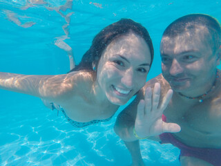 Happy couple smiling underwaterin pool with blue water