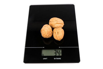 Three walnuts in the shell on a digital scale isolated over white