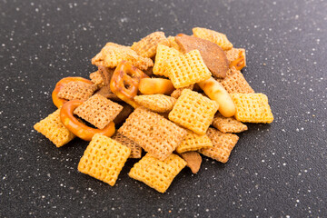 Cereal holiday mix with pretzels and crunchy salty pieces in a bowl isolated over black