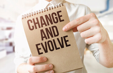 Text Change and Evolve on brown paper notepad in businessman hands in office. Business concept