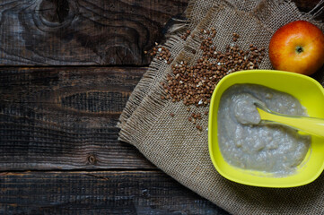 baby buckwheat puree porridge in a bright light green silicone plate with a spoon on an old rustic background, copy space and top view, baby's first feeding, healthy eating concept
