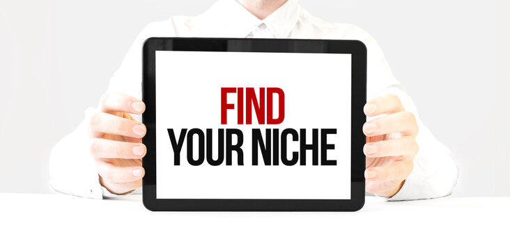 Text FIND YOUR NICHE on tablet display in businessman hands on the white bakcground. Business concept