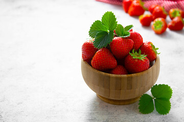 Fresh strawberries in wooden bowl with green leaves. Copy space.