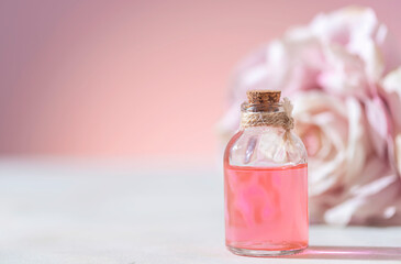 Perfumed Rose Water or essential oil in glass bottle and rose flower on a light background.