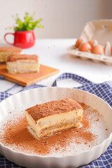 Delicious Tiramisu - traditional italian dessert from mascarpone cheese and biscuit. gourmet tiramisu dessert topped with chocolate powder served on a white plate at table background.