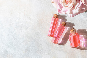 Perfumed Rose Water or essential oil in glass bottle and rose flower on a light background.