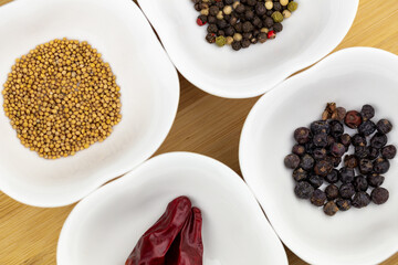 Chilli peppers and a selection of pepper seeds, juniper seeds and mustard seeds on white bowl on a chopping board