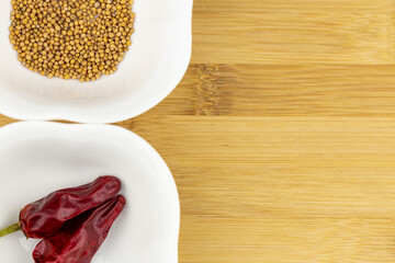 Chilli peppers and mustard seeds on white bowl on a chopping board