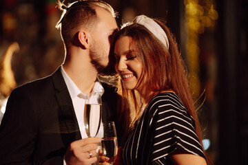 Young happy couple in love toasting with champagne on the bar. Smiling man and woman clinking a glass champagne, enjoying winter holiday. Party, celebration, drink, birthday concept.