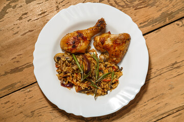 Marinated baked chicken drumsticks and wings with risotto in a plate on the table.