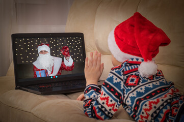Kid in santa hat is having web chat call with Santa. Boy listening Santa Claus online.