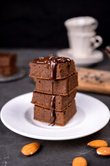 Cocoa brownies pouring with melted dark chocolate on a white plate. Black background