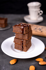 Cocoa brownies pouring with melted dark chocolate on a white plate. Black background