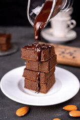 Cocoa brownies pouring with melted dark chocolate on a white plate. Black background