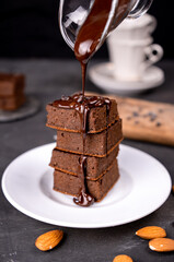 Cocoa brownies pouring with melted dark chocolate on a white plate. Black background