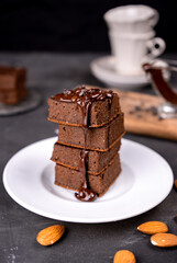 Cocoa brownies pouring with melted dark chocolate on a white plate. Black background