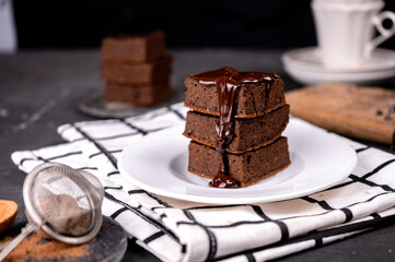 Cocoa brownies pouring with melted dark chocolate on a white plate. Black background