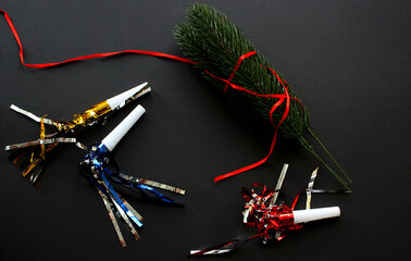 Bunch of green spruce lush twigs wrapped in a red ribbon on a black background. Shiny festive air whistles. Christmas tree. Top view. Celebration. New Year 2021. Copy space.
