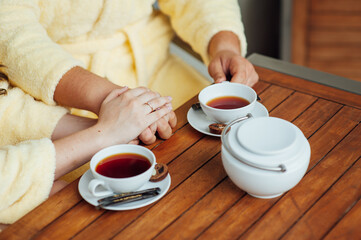 A loving couple sits in dressing gowns and drinks tea on a wooden table