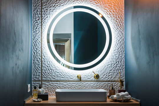 Modern Bathroom Interior With White Wash Basin, Golden Faucet And Round Illuminated Mirror.