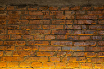 Background of old vintage red brick wall with concrete, illuminated from below with yellow light, dried up bricks texture, Grunge background