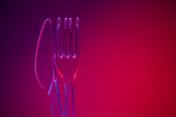 Plastic transparent fork and knife on red background