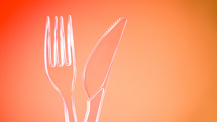 Plastic transparent fork and knife on orange background