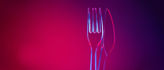 Plastic transparent fork and knife on red background