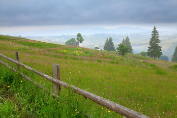 Fototapeta na wymiar Mountain landscape, view of the village and mountains, meadow and wooden fence in the foreground. Uraine, Carpathians.
