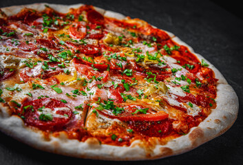 Pizza with Mozzarella cheese, ham, tomato sauce, pepper, salami. Italian pizza on Dark grey black slate background