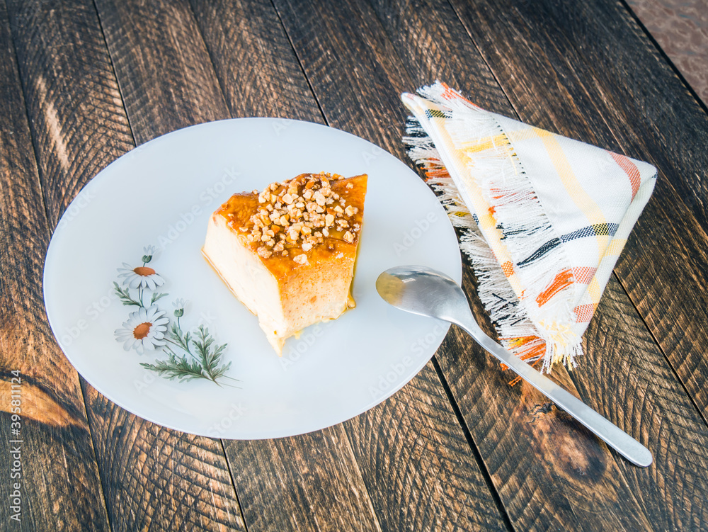 Wall mural Piece of nougat creme caramel  on a plate with a striped napkin and a spoon on a wooden table