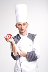 Smiling chef is holding apple on copyspace. Chef showing fruit. Pleased happy young chef posing isolated over white wall background in uniform.
