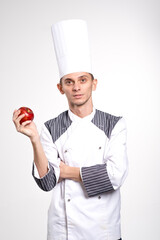 Smiling chef is holding apple on copyspace. Chef showing fruit. Pleased happy young chef posing isolated over white wall background in uniform.