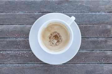 Frosty morning with coffee outside. White cup of cappuccino on a frozen rustic wooden table. Freshly fall winter background.