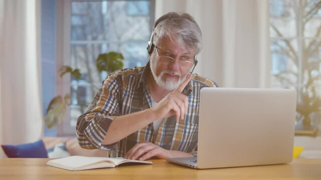 Aged man with headset and laptop computer having video conference at home office