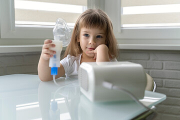 cute little girl holding a nebulizer mask in her hands. treatment of bronchitis and asthma with...