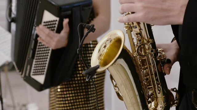Cool saxophonist performing duet with accordionist, musician playing in jazz band - close-up