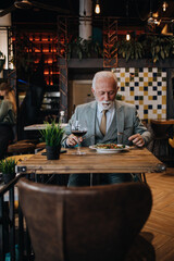 Happy businessman sitting in restaurant and having lunch. He is enjoying in delicious food and wine.